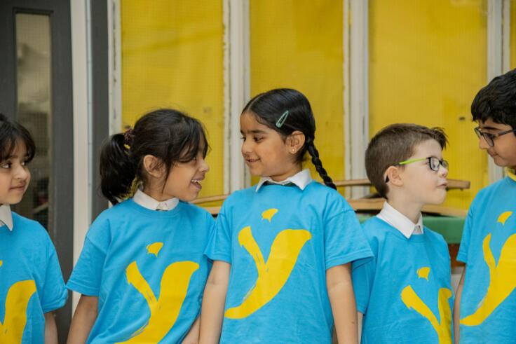 A group of children wearing Y Dance t-shirts look at each other smiling.